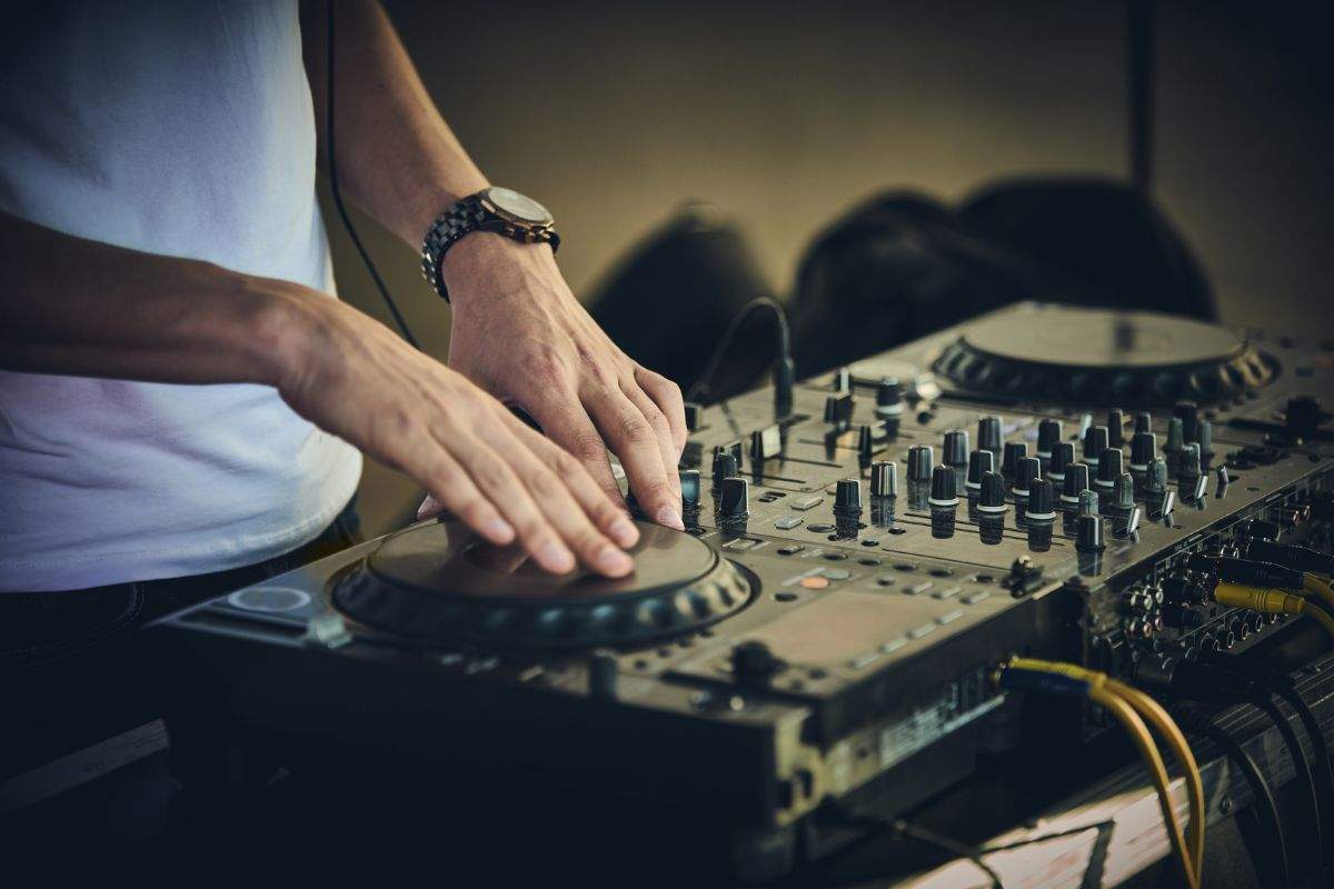 A close-up of a DJ's hands operating a professional mixing console and turntable.