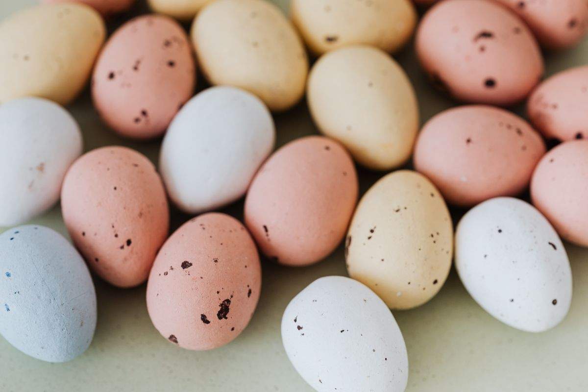 A scattered collection of pastel-coloured, speckled chocolate eggs.