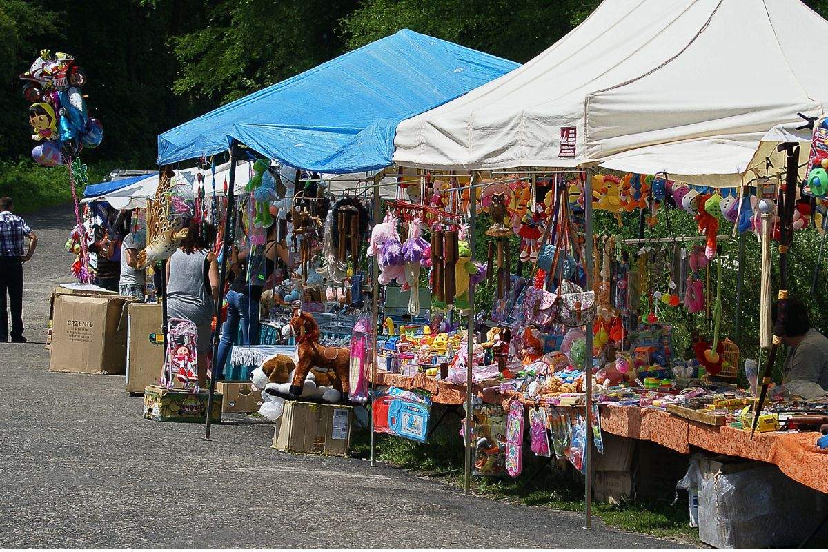 Outdoor market stalls under blue and white canopies filled with toys, stuffed animals, and colourful merchandise.